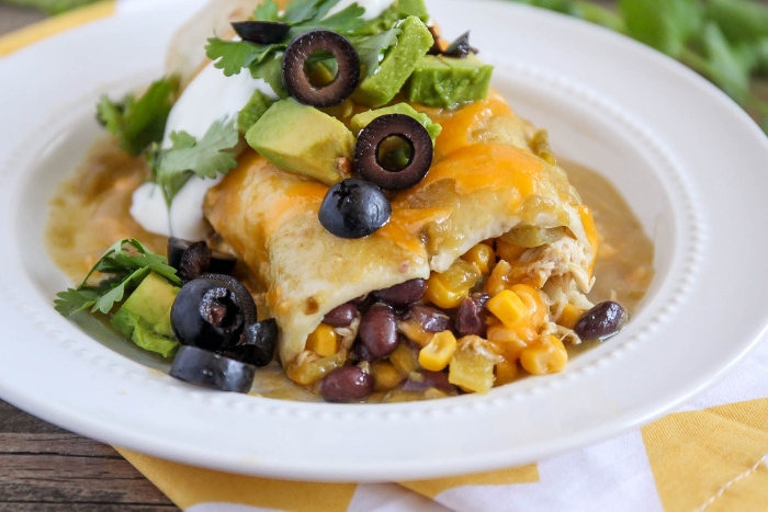 smothered burrito on a white plate topped with sour cream, olives, and avocado