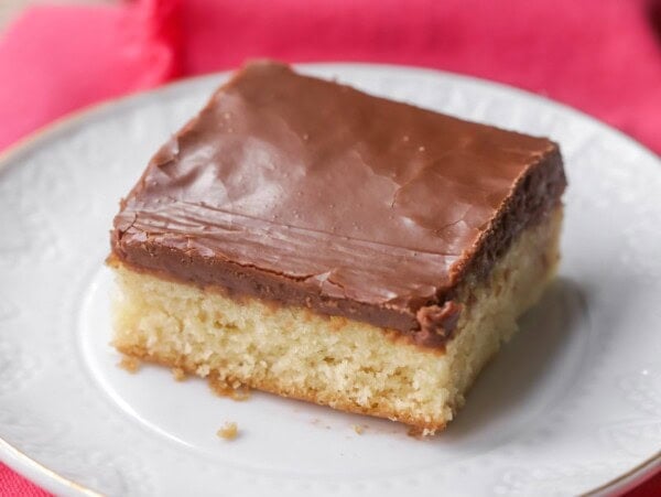 A slice of white sheet cake with chocolate frosting on a plate.