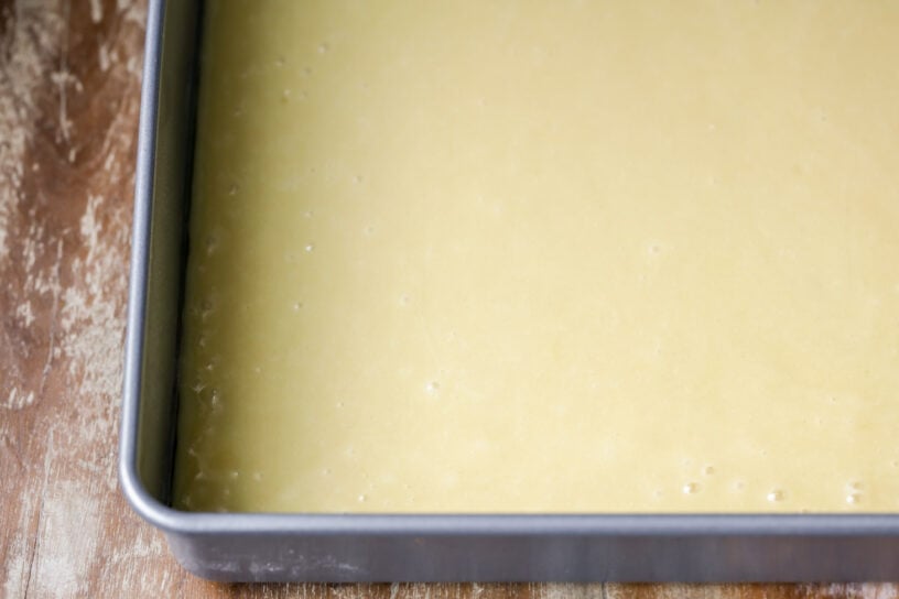 This White Sheet Cake with Chocolate Frosting is easy to make, melts in your mouth, and is always a crowd pleaser! White cake batter in a metal cake pan ready to be baked to make white sheet cake with chocolate frosting.