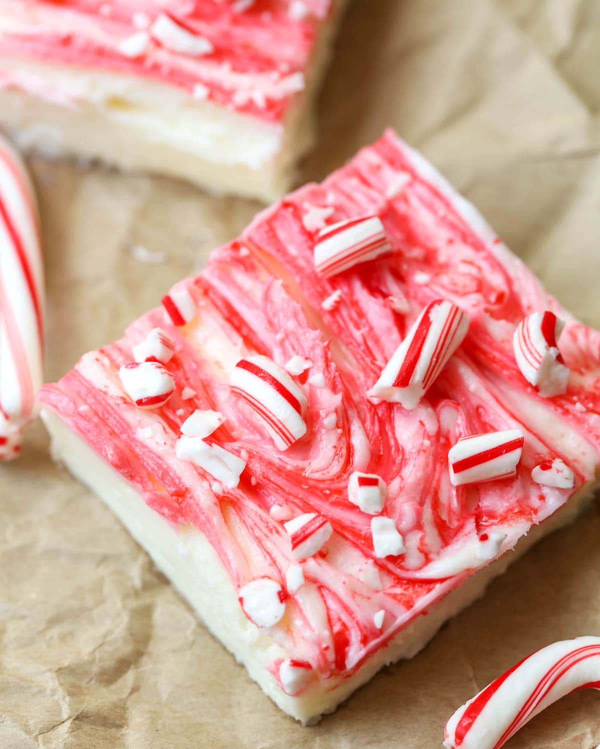 Candy cane topped peppermint cheesecake bars on brown paper.