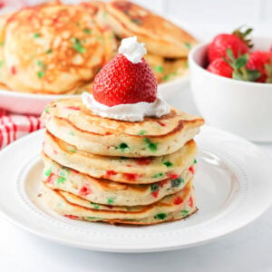 Christmas Pancakes stacked on white plate with strawberry Santa hats.