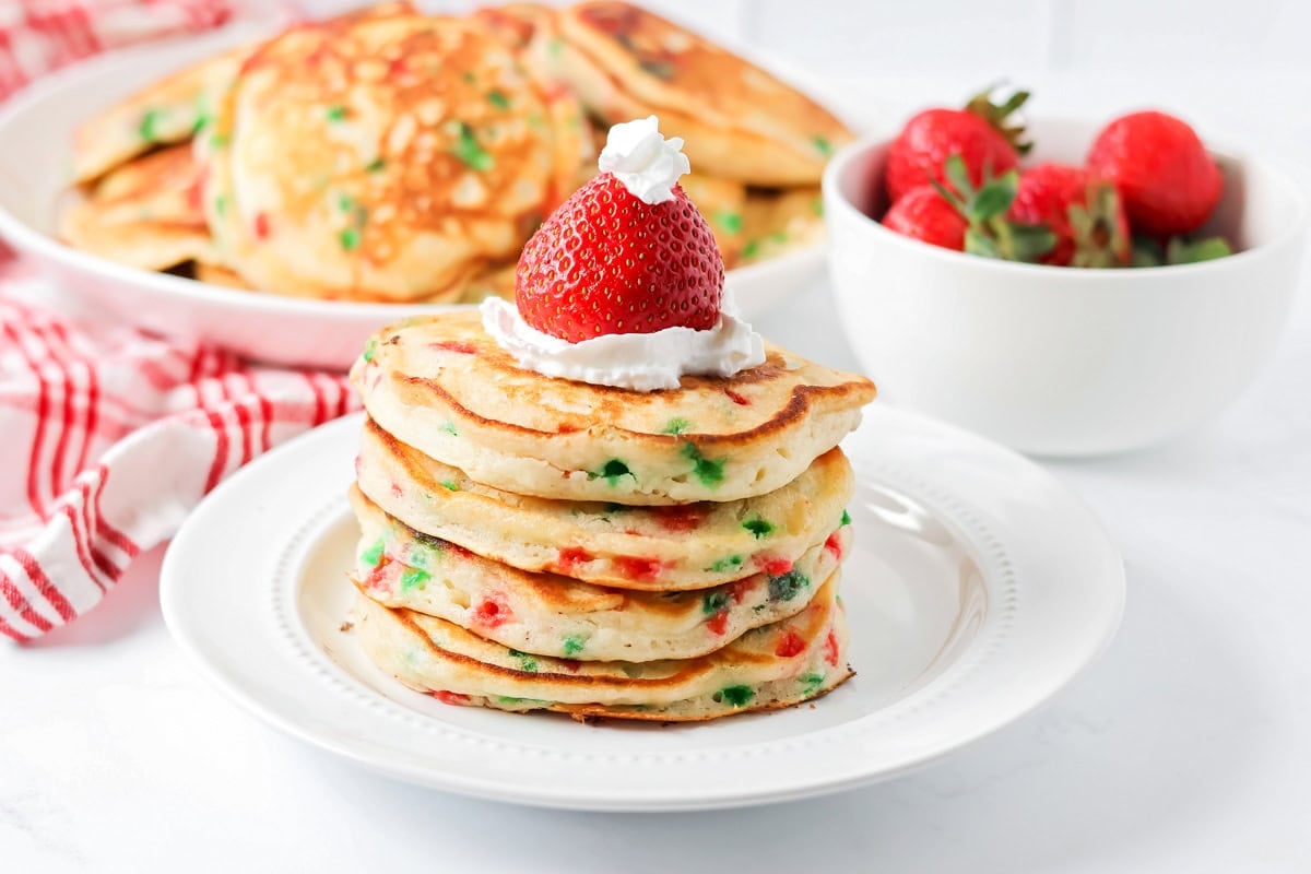 Christmas Pancakes stacked on white plate with strawberry Santa hats.