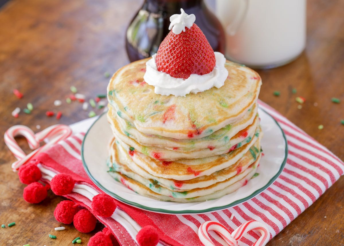 Christmas pancakes filled with sprinkles and stacked on a white plate.