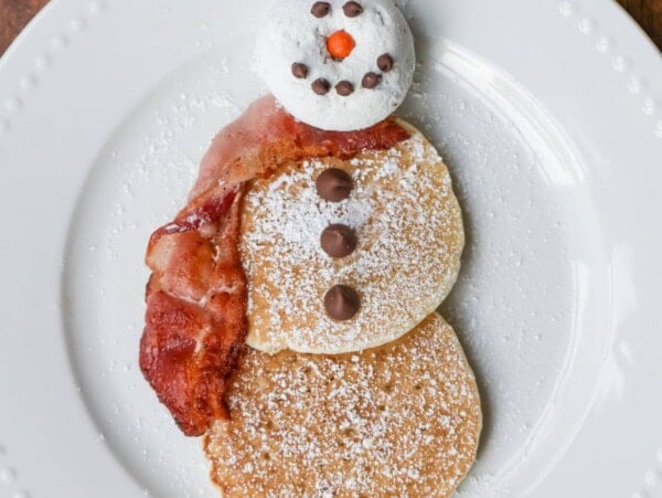 Snowman Pancakes are a fun Christmas breakfast made with pancakes, donuts, bacon, candy and powdered sugar.