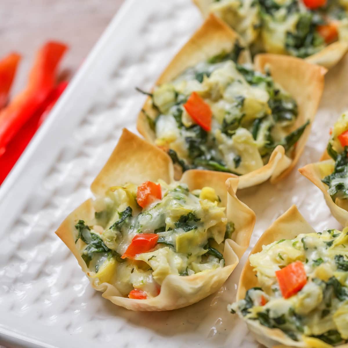 Finger food appetizers - 3 spinach artichoke cups on a white plate.