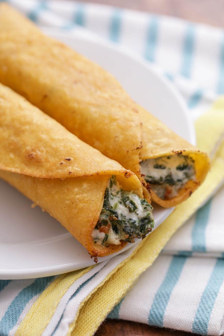 Cheesy spinach and artichoke taquitos served on a white plate