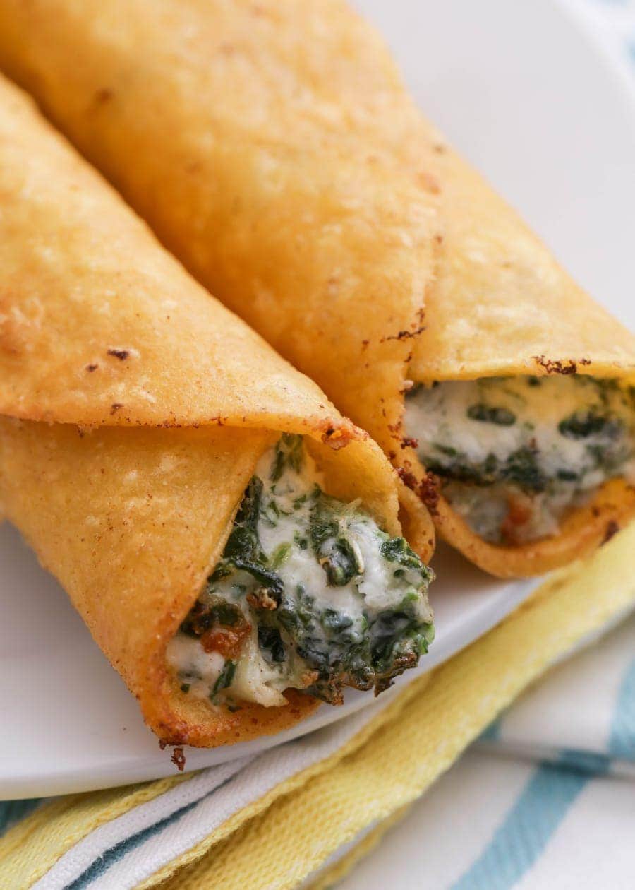 Cheesy Spinach and Artichoke Taquitos fried and served on a white plate