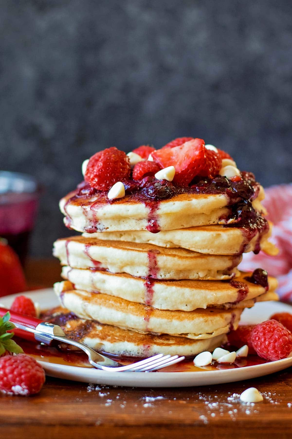 Stack of white chocolate berry pancakes served on a white plate topped with berry sauce