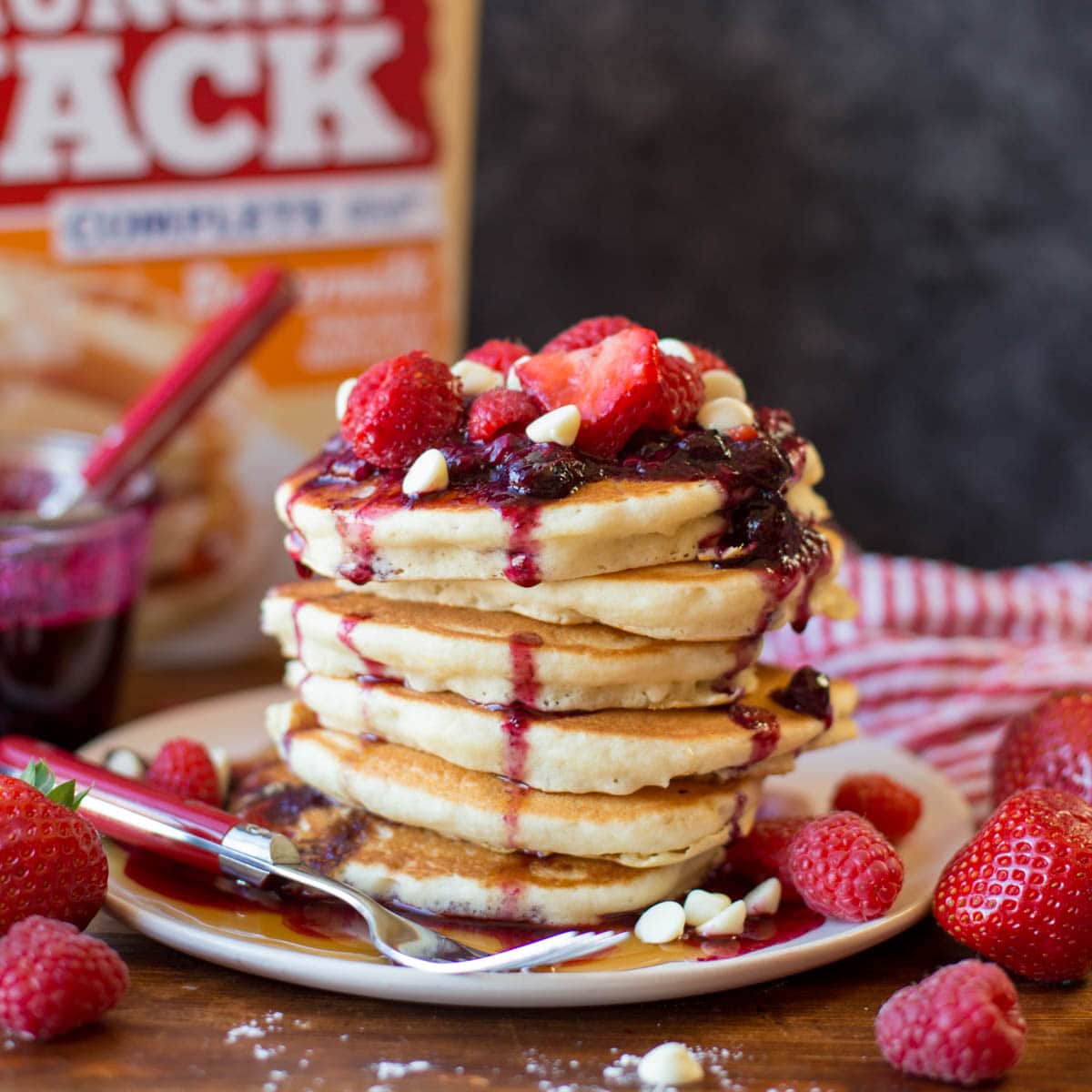 Stack of white chocolate berry pancakes topped with berry syrup