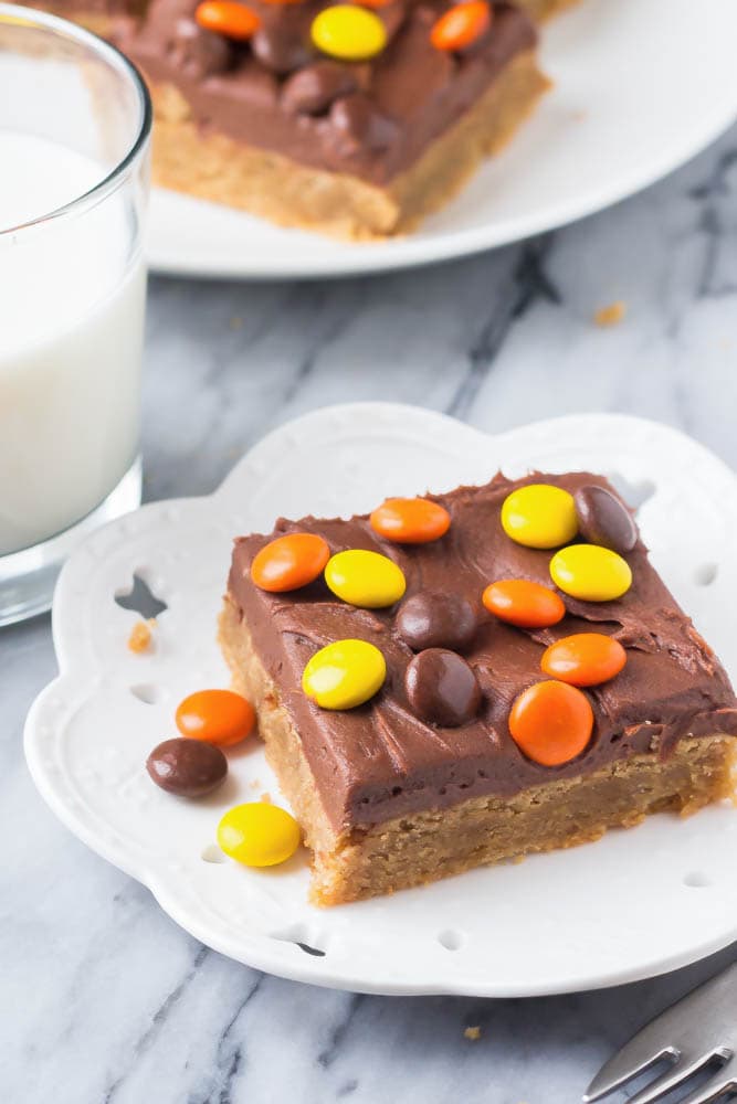 Chocolate peanut butter cookie bar topped with reese's pieces on a white plate