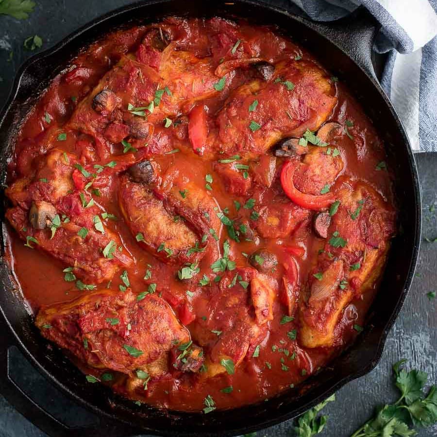 boneless chicken being cooked in crushed tomatoes in skillet for chicken cacciatore recipe