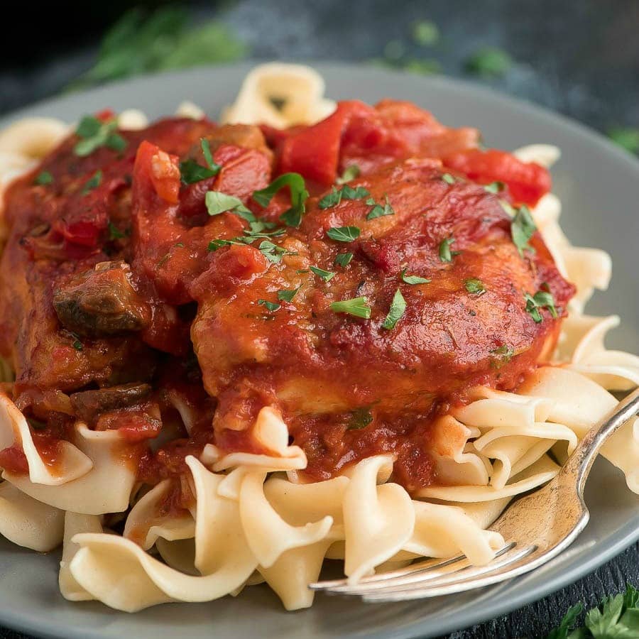 Finished Chicken Cacciatore served over pasta on grey plate