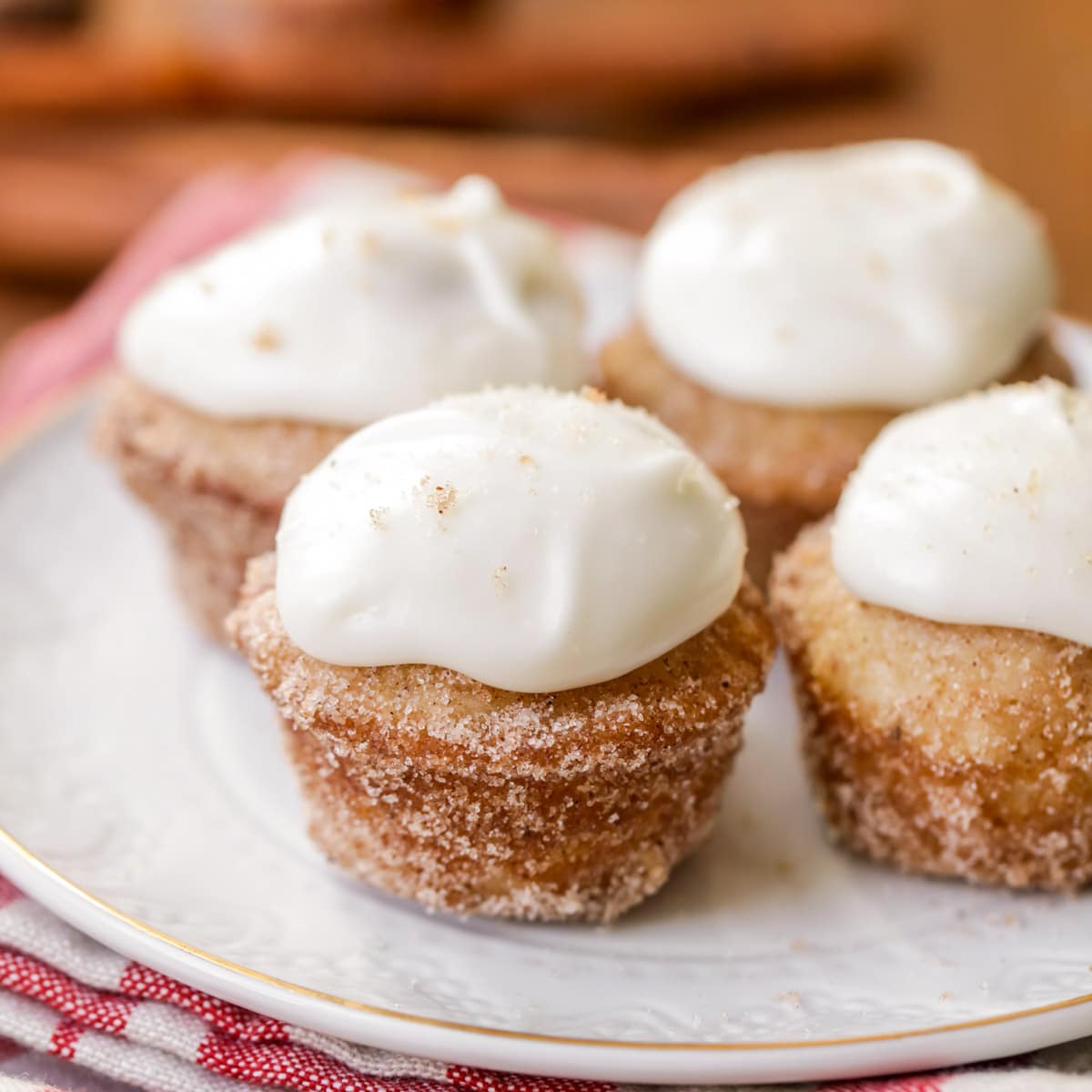 Mini donut muffins with white frosting on a gold rimmed white plate. 