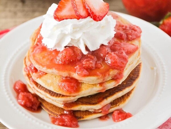 stack of strawberry pancakes with whipped cream and strawberry on top
