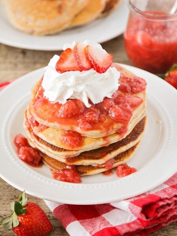 stack of strawberry pancakes with whipped cream and strawberry on top