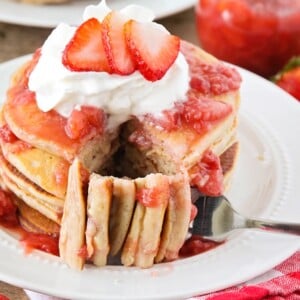 Strawberry pancakes topped with fresh whipped cream and strawberries with a bite missing.