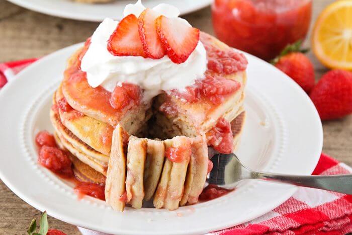 Strawberry pancakes on a white plate with a piece cut out