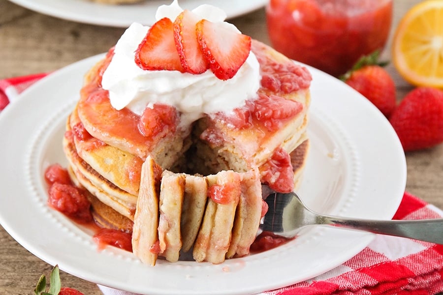 Stack of strawberry and cream pancakes on white plate