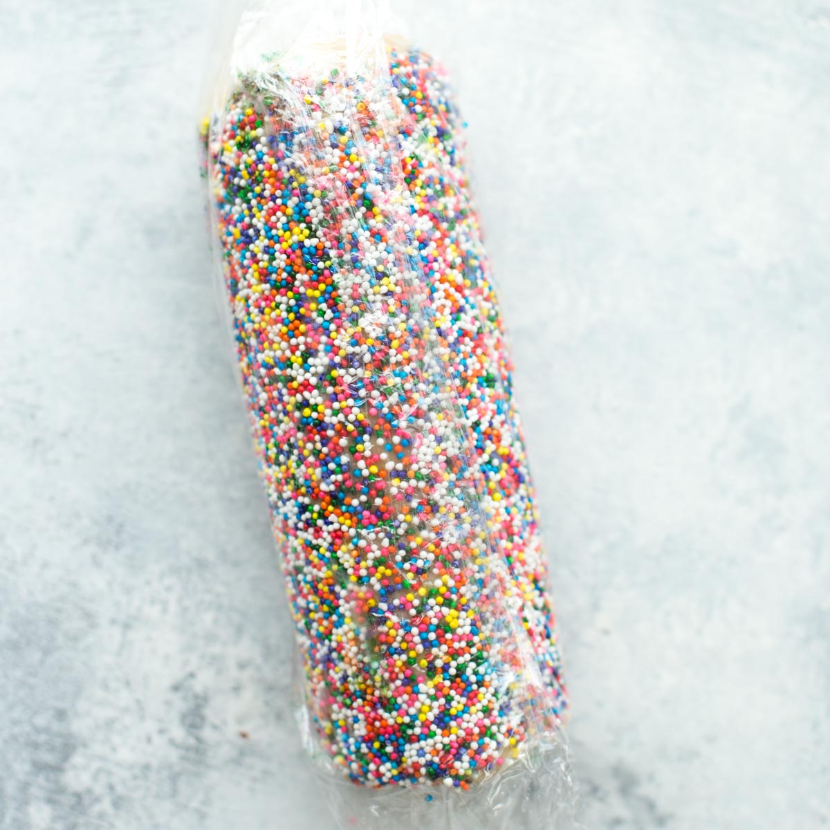 Cookie dough log with sprinkles on the outside wrapped in plastic wrap for St. Patrick's Day slice and bake cookies