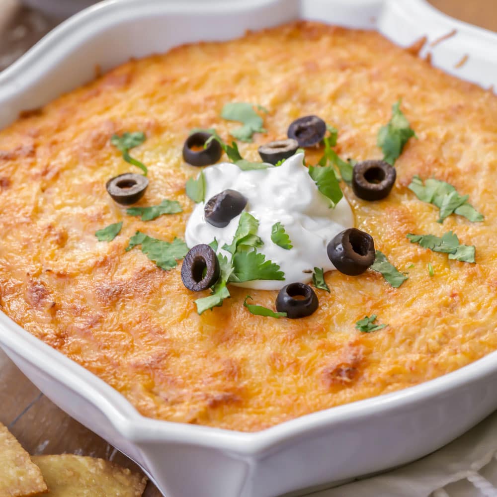 Appetizer Dips - Tamale Dip in a white serving dish garnished with sour cream, sliced black olives, and chopped cilantro. 