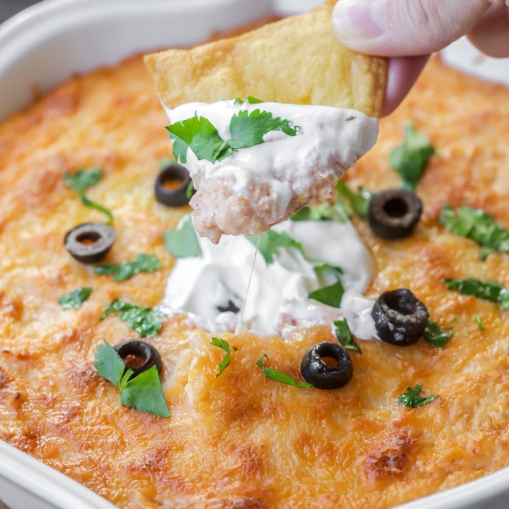 Crock Pot Appetizers - Tamale Dip topped with melted cheese, cilantro, cream cheese, and sliced black olives in a white serving dish. 