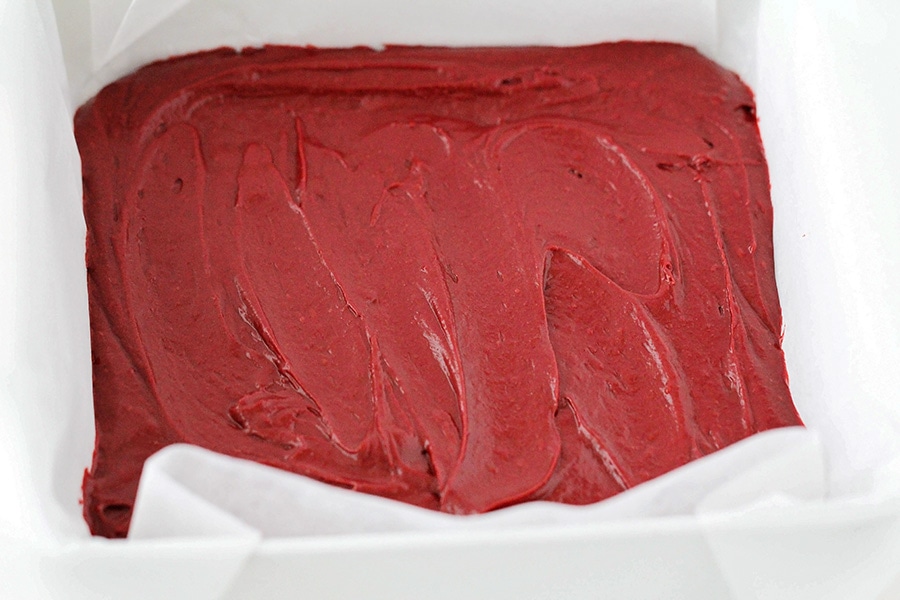 Spreading batter for red velvet cheesecake brownies in a pan.