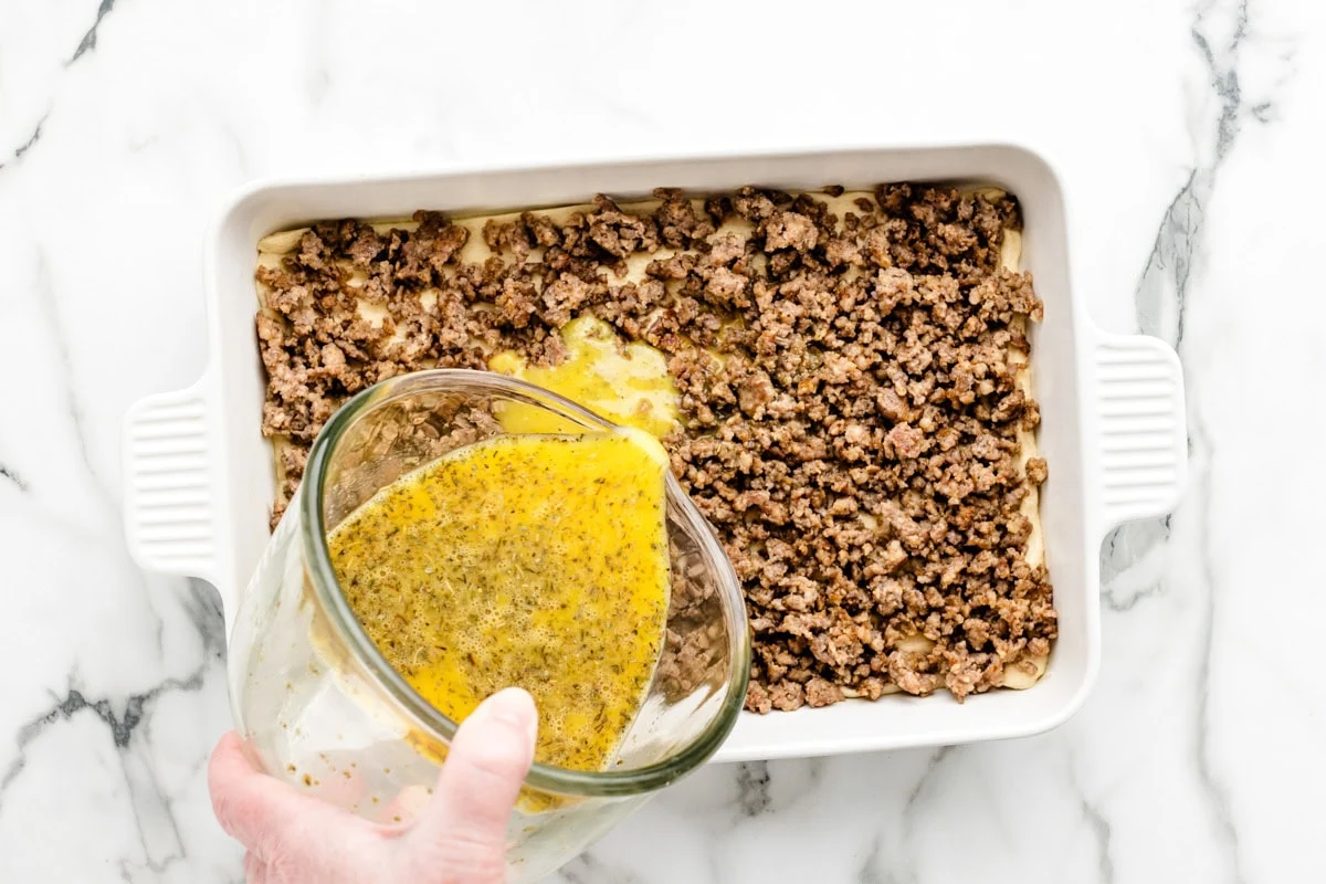 Pouring the egg mixture over the sausage for the breakfast casserole.