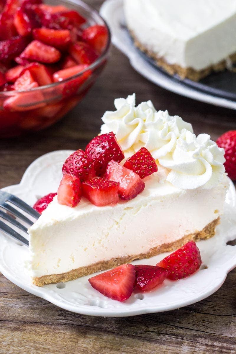 A close up of a slice of no bake cheesecake topped with diced strawberries.