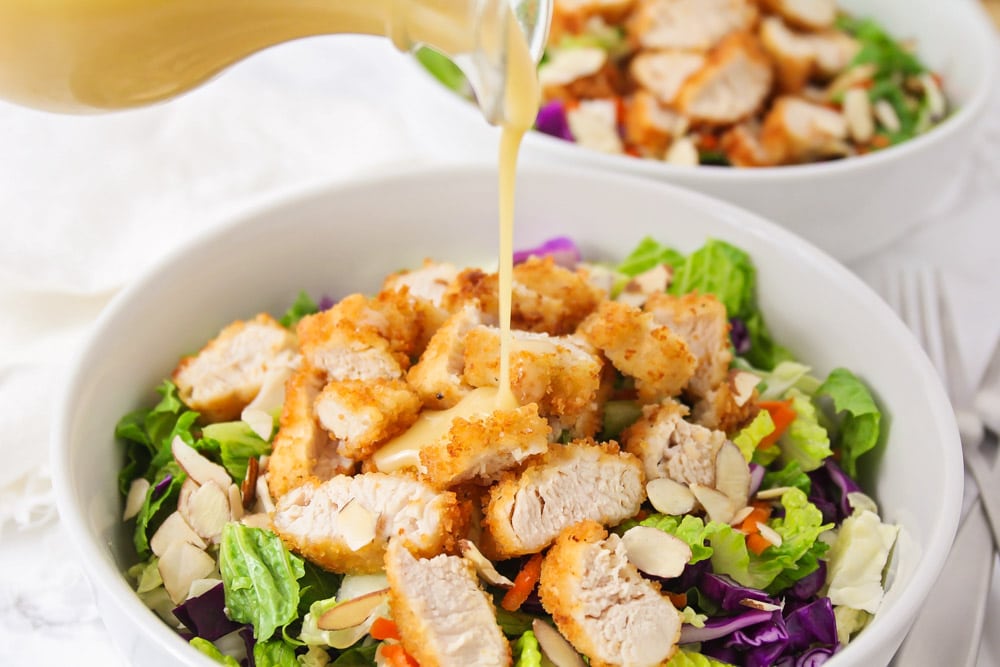 Healthy Dinner Ideas - Oriental Chicken Salad in a white bowl with dressing pouring on the top.