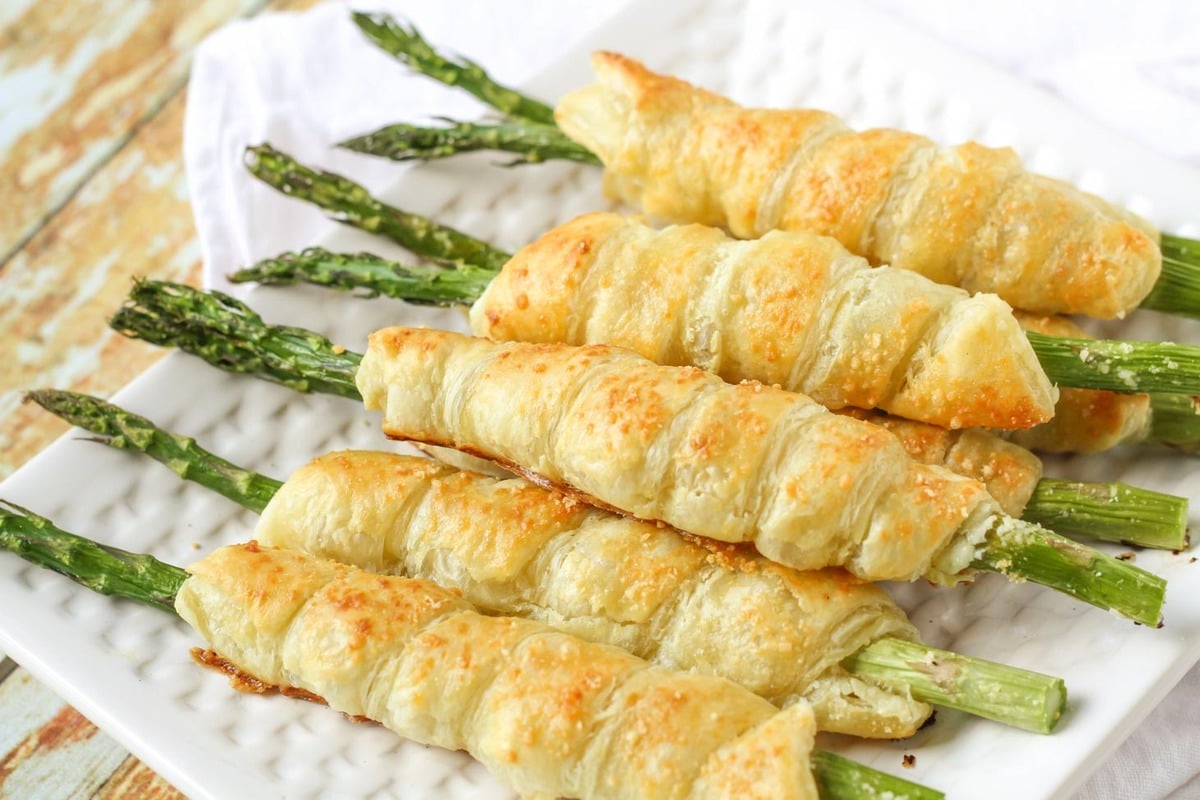 Thanksgiving appetizers - puff pastry wrapped asparagus rolls piled on a plate.