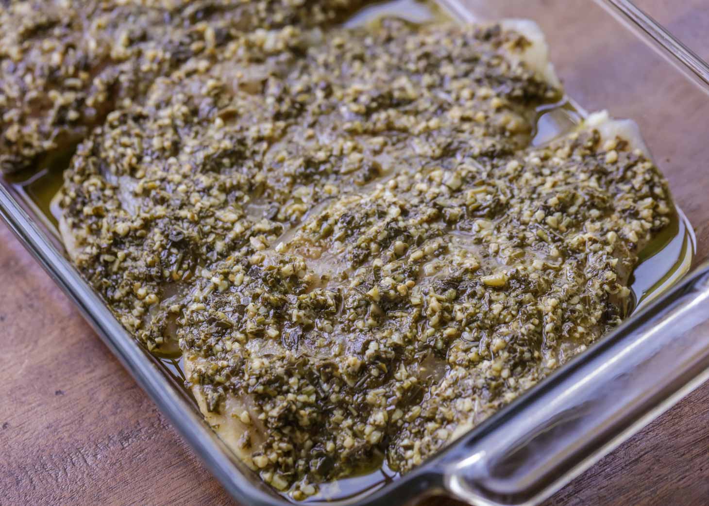 Chicken breasts covered with basil pesto in a baking dish for making baked pesto chicken.