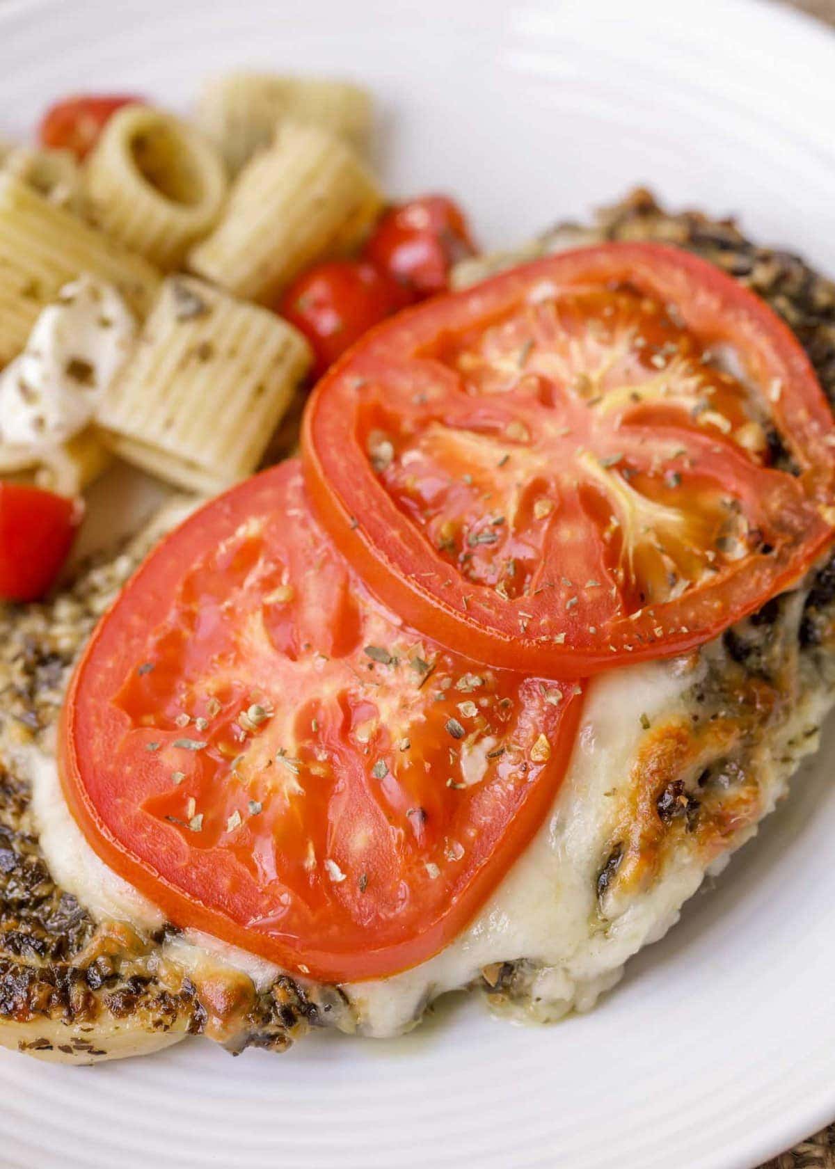 Baked pesto chicken on a plate served with pasta.