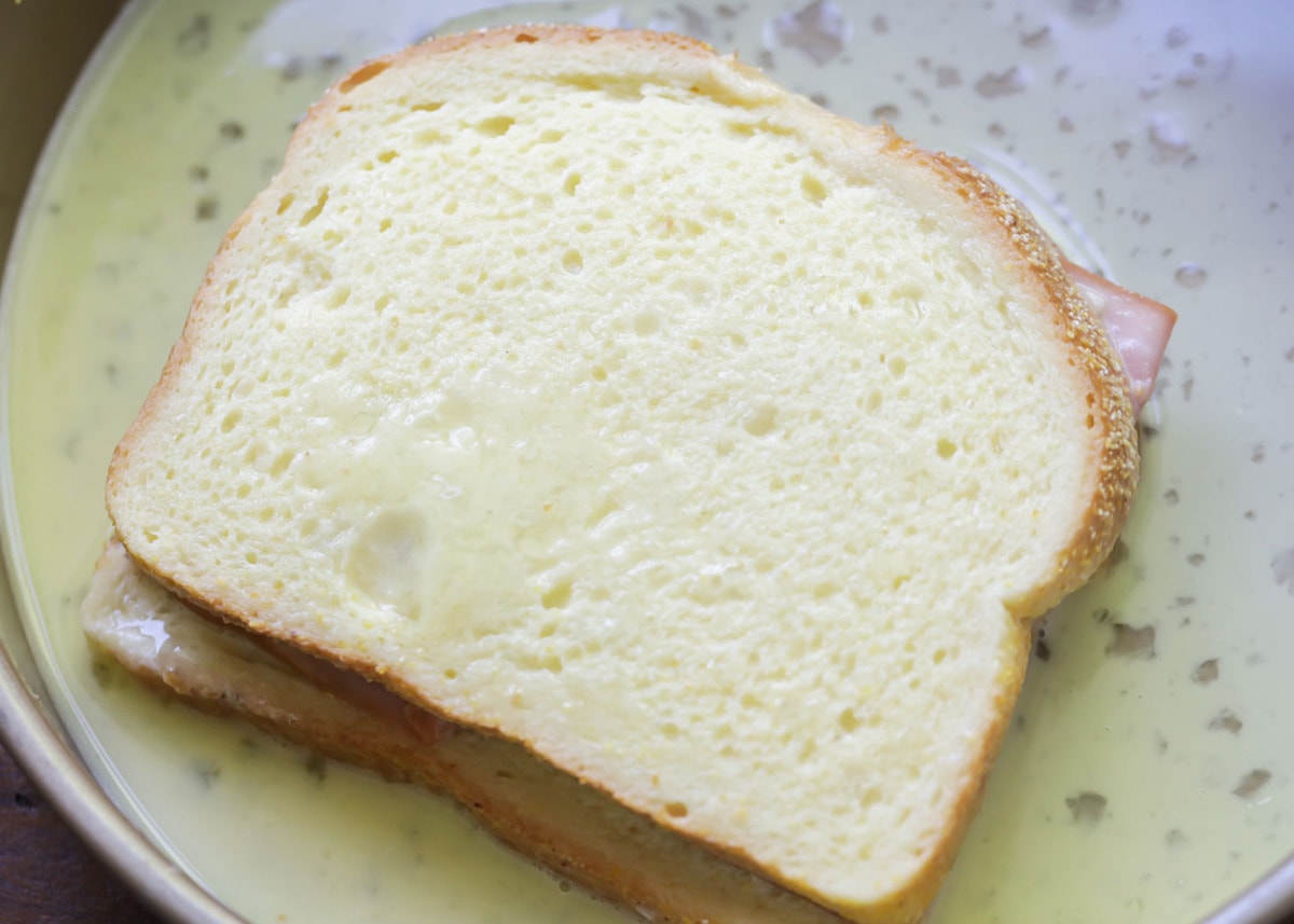 Dipping Croque Monsieur sandwich in egg mixture.