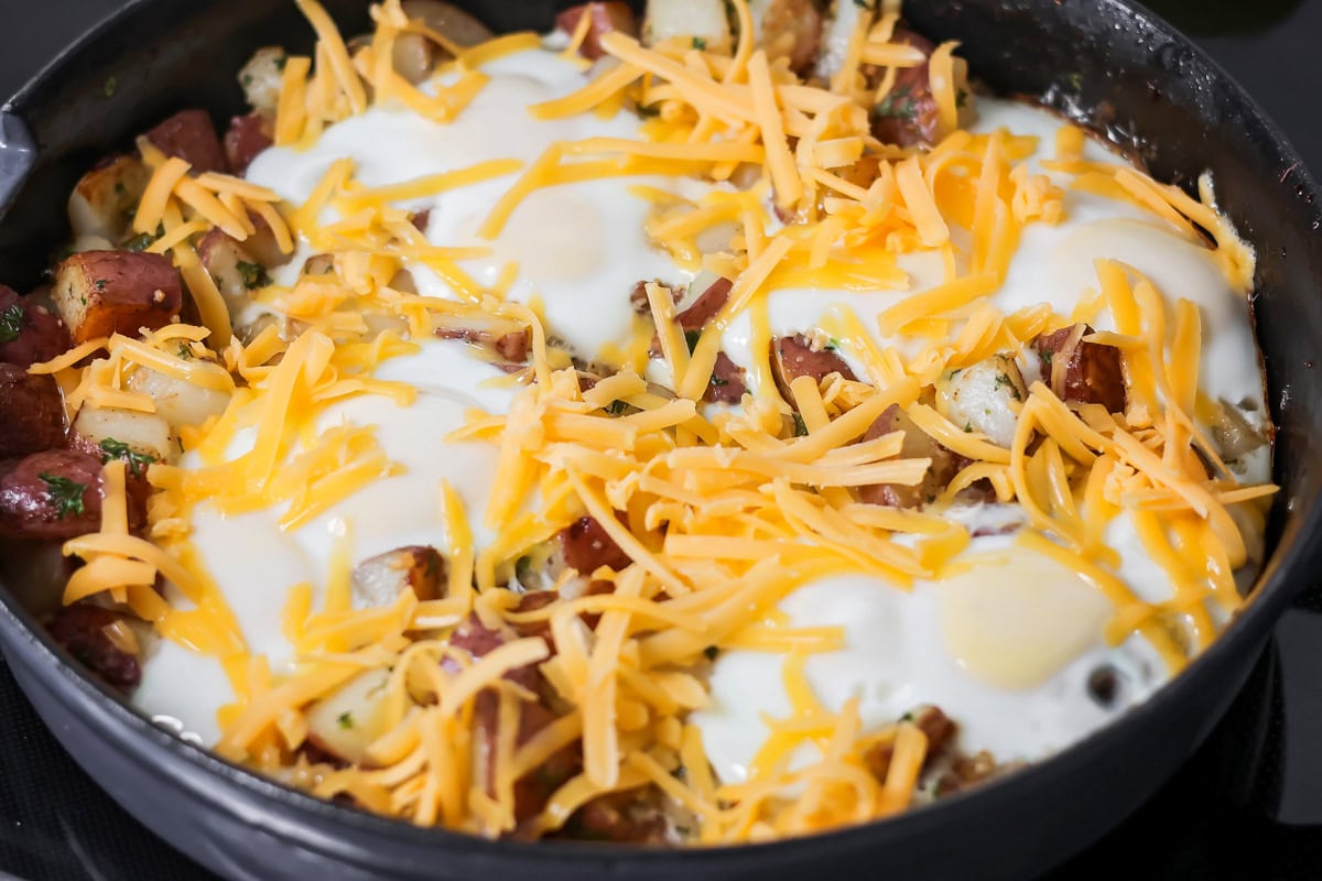 Eggs and potatoes cooked in skillet with cheese sprinkled on top.