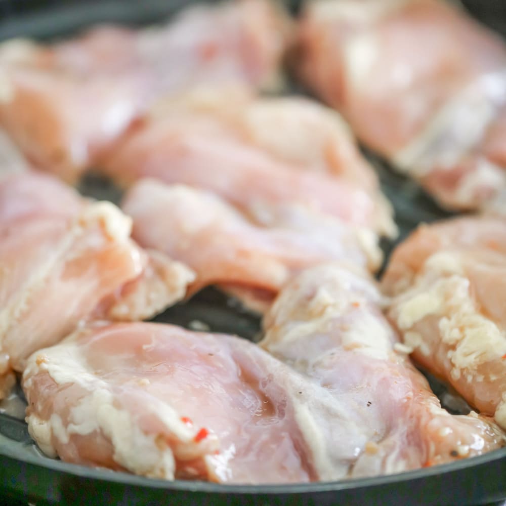 Raw chicken thighs cooking in a skillet.