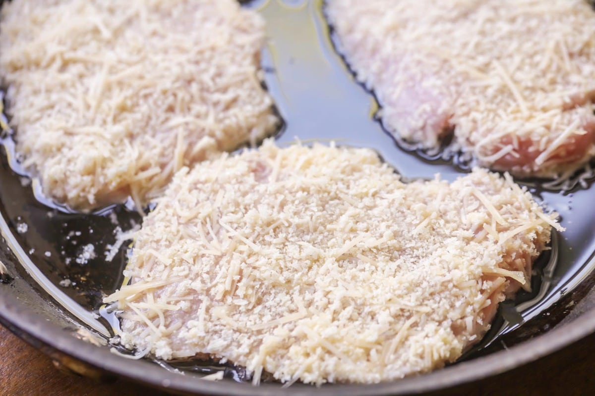 Breaded pork chops frying in a cast iron skillet.