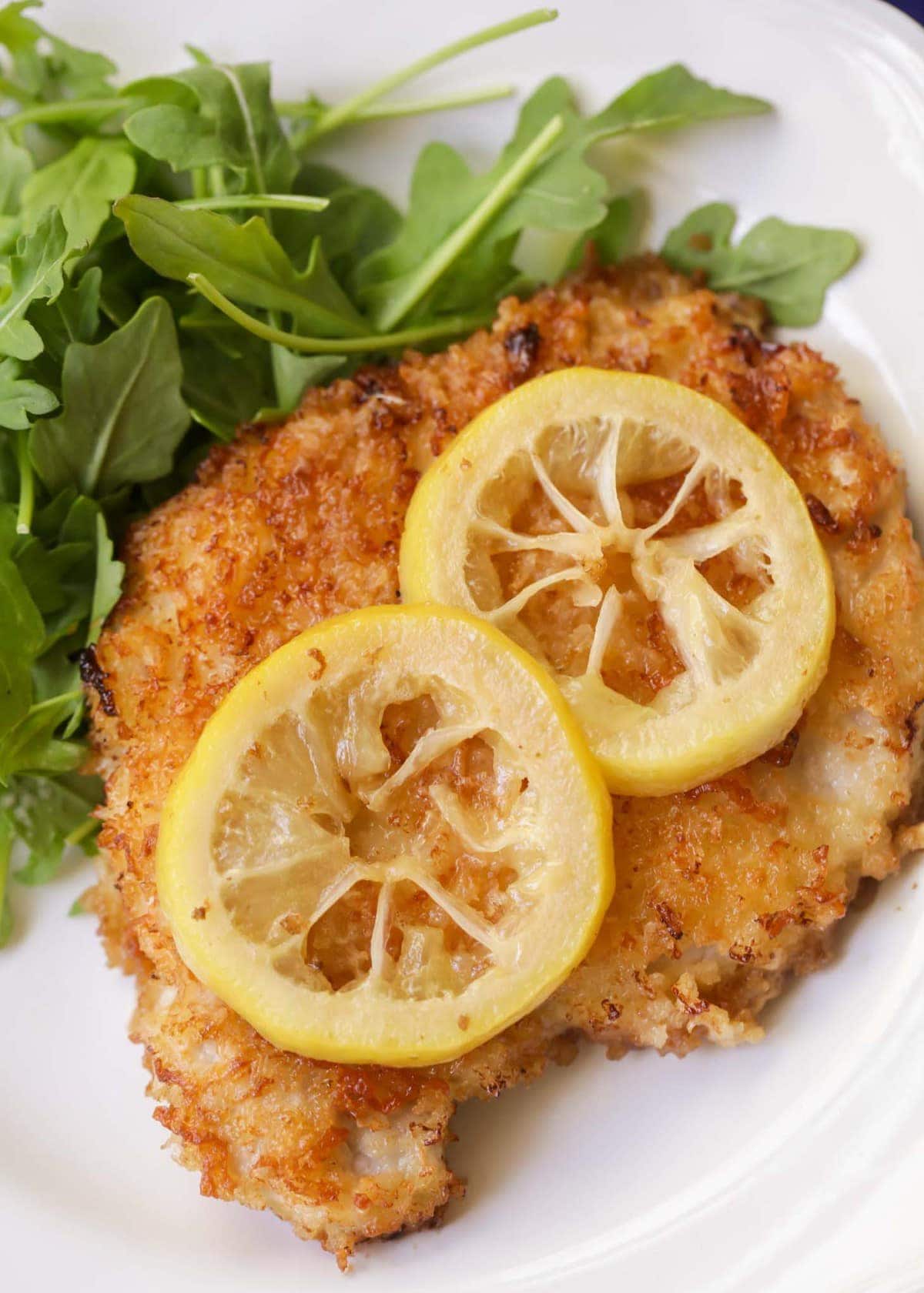 Pan fried pork chops with lemon slices served on a white plate.