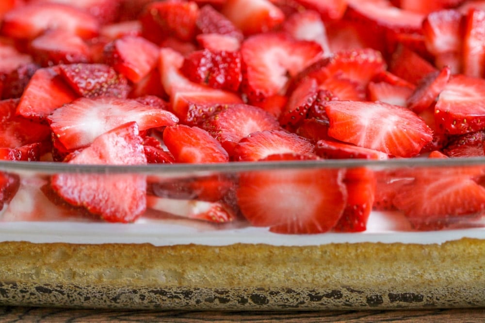 Strawberry shortcake dessert bar in a glass baking dish topped with fresh sliced strawberries.