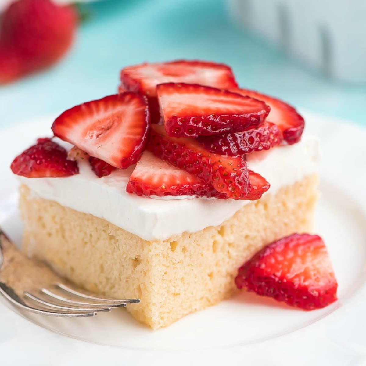 A slice of tres leches cake topped with fresh strawberries