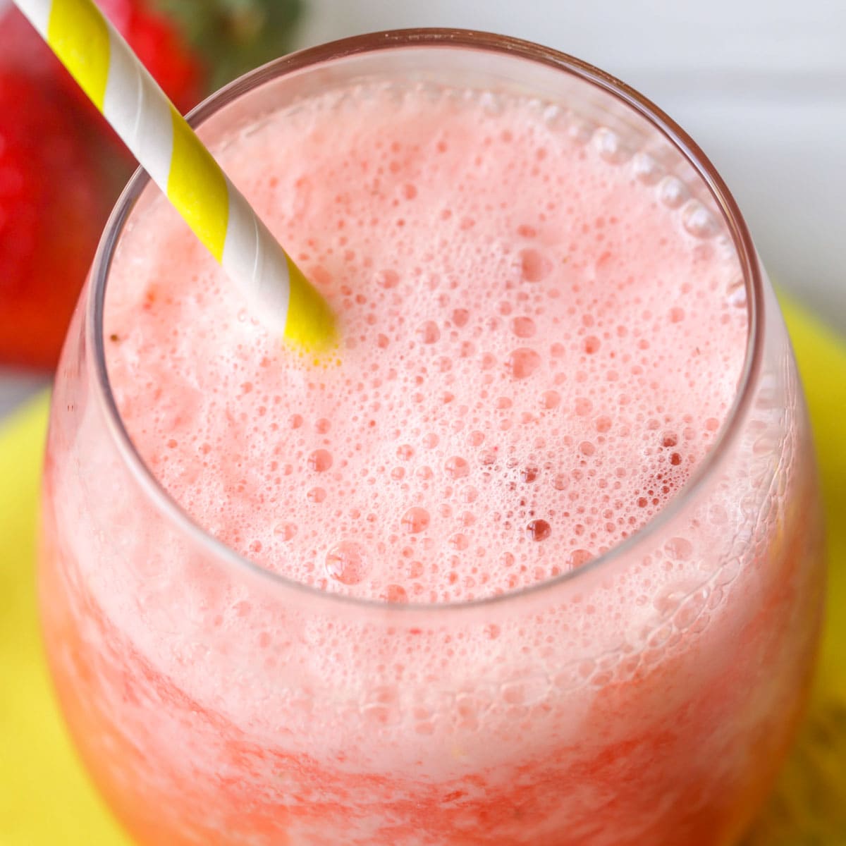 Frozen strawberry lemonade served in a glass with a yellow straw.