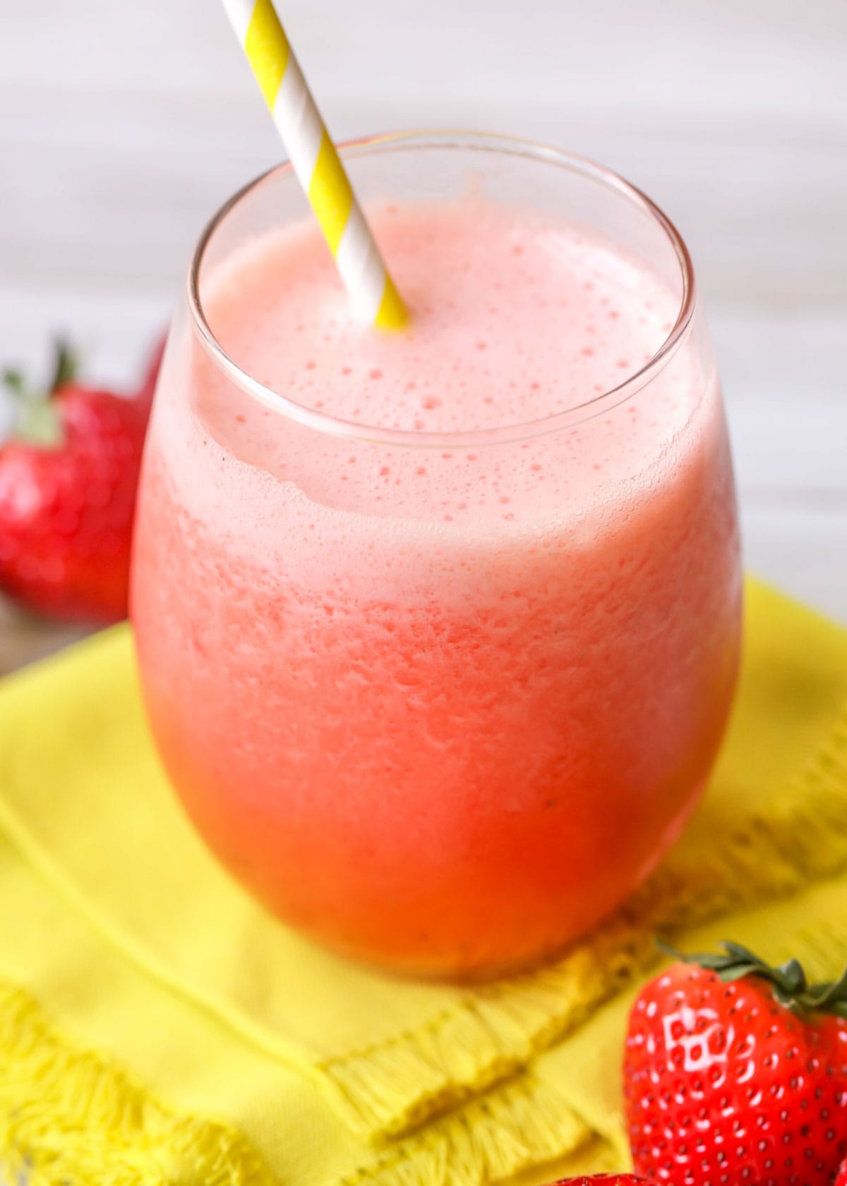 A glass full of frozen strawberry lemonade with a yellow straw.