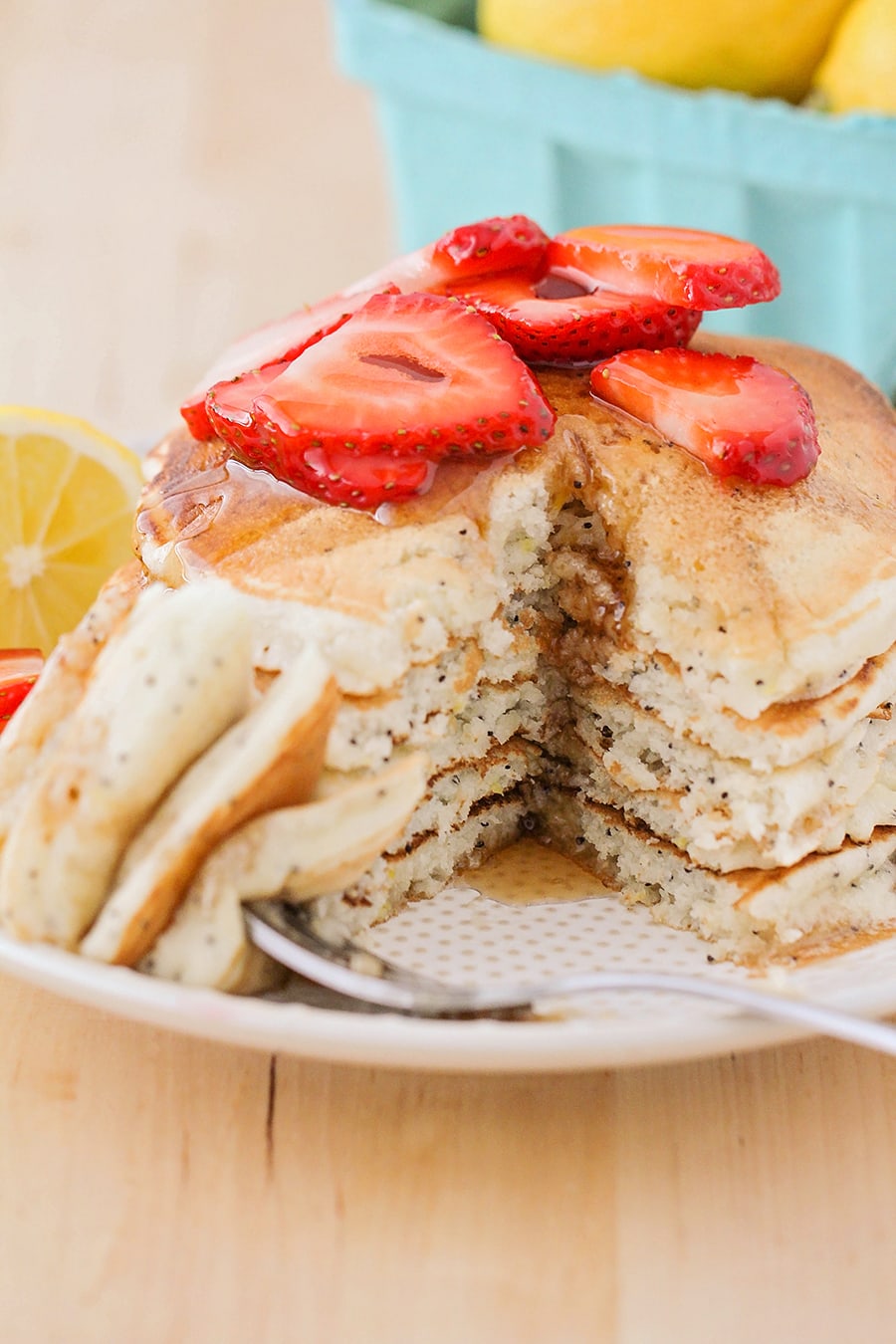Lemon poppyseed pancakes topped with strawberries and syrup on a white plate