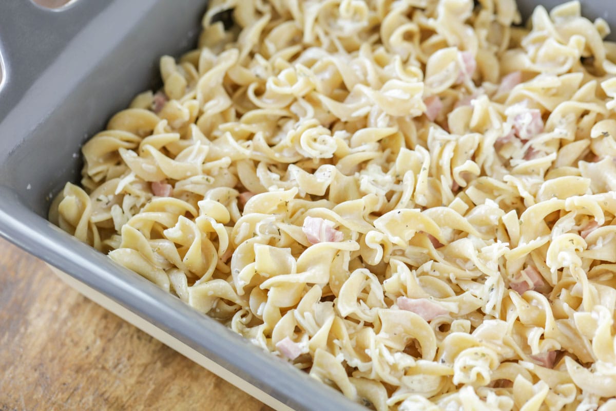 egg noodles covered in cheese and ham in a baking dish