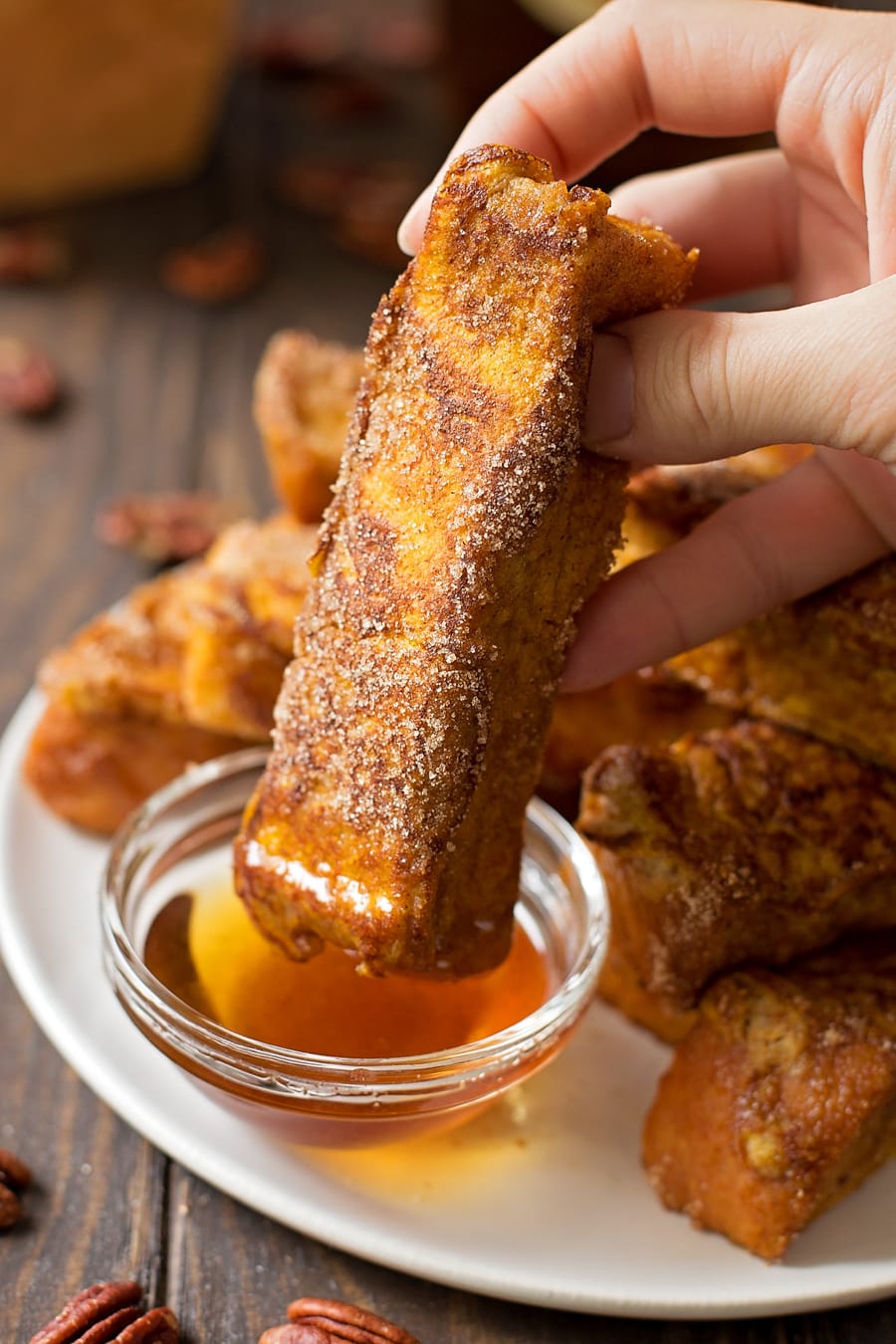 hand dipping a french toast stick in syrup