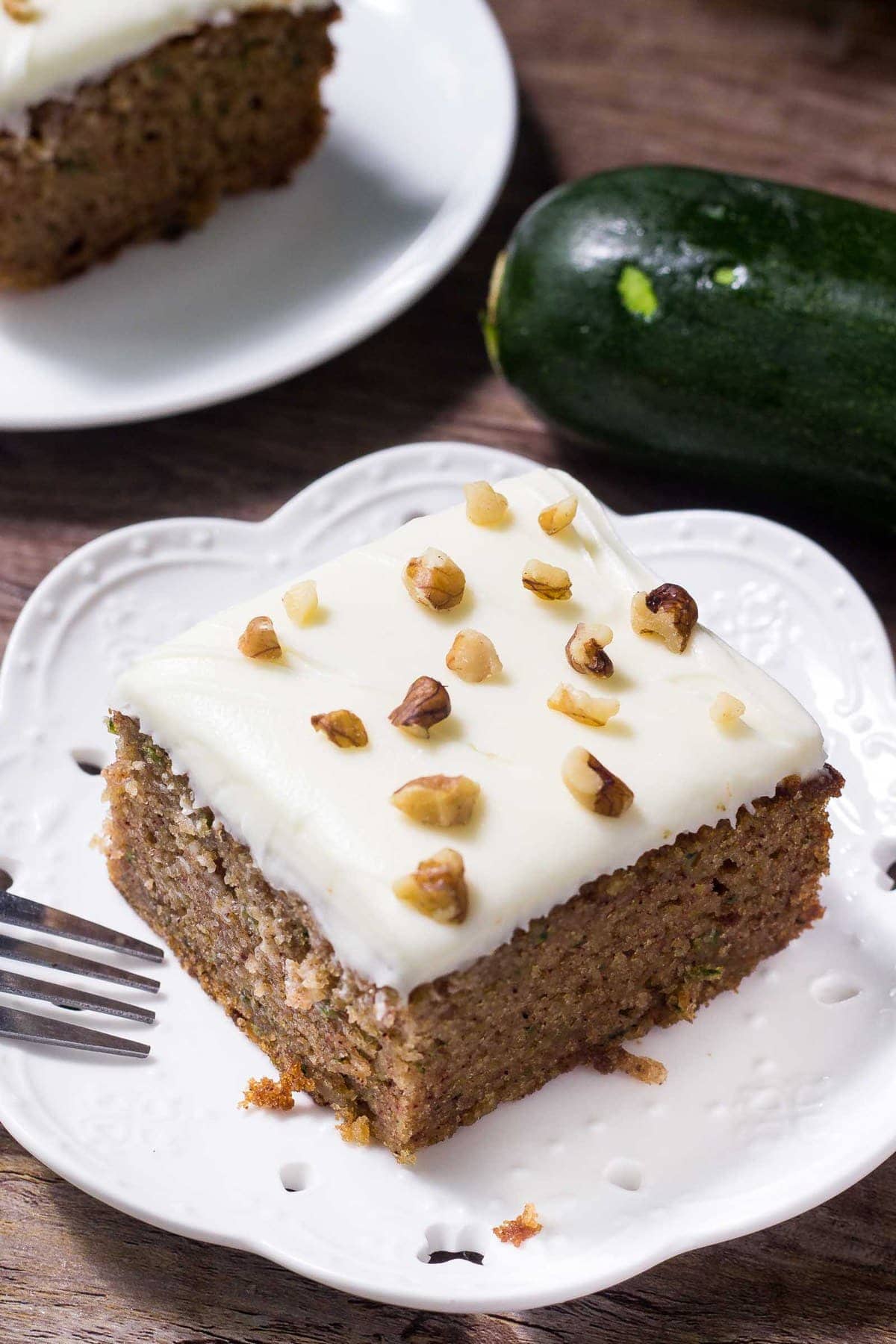 Zucchini cake topped with frosting and walnuts on a white plate