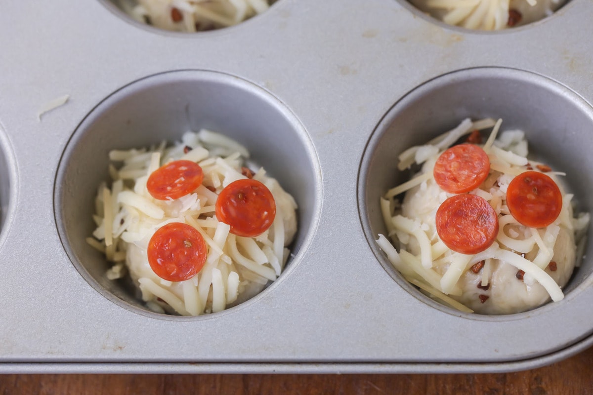 Muffin tin pizzas topped with mini pepperonis ready to be baked. 