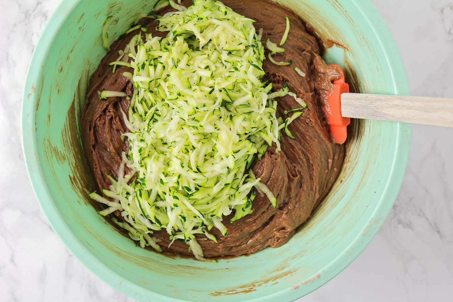 Adding grated zucchini to chocolate batter in a mint bowl.