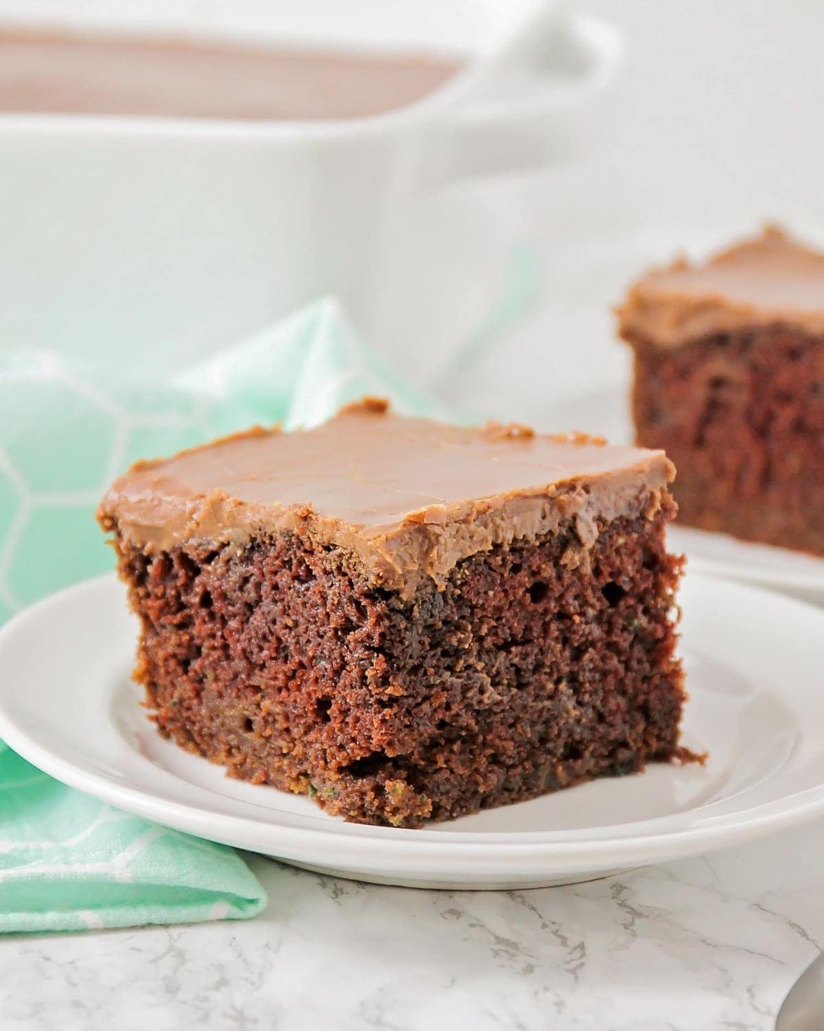 A close up of a slice of chocolate zucchini cake topped with chocolate frosting.