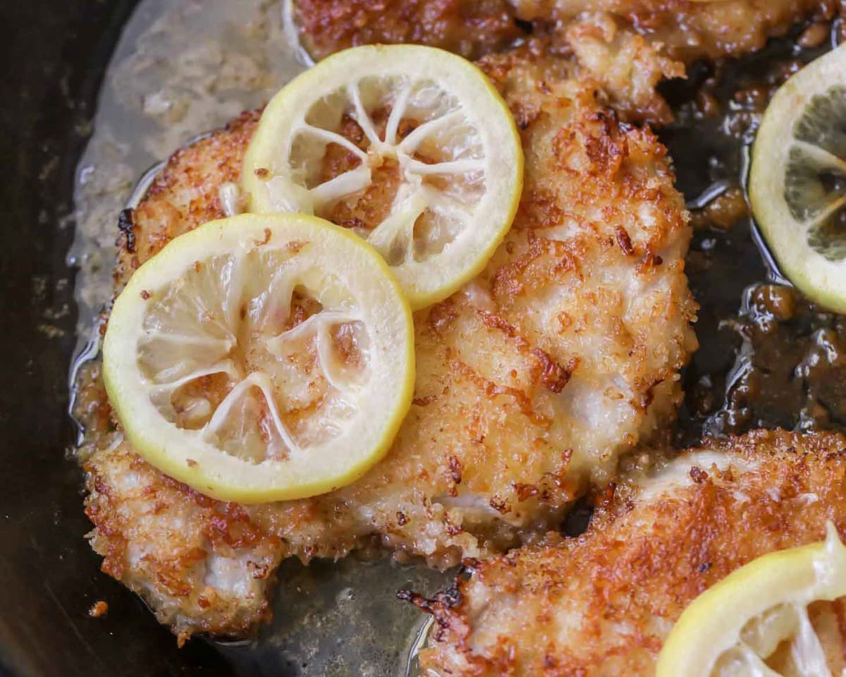 Fried pork chops with lemon cooking in a frying pan.