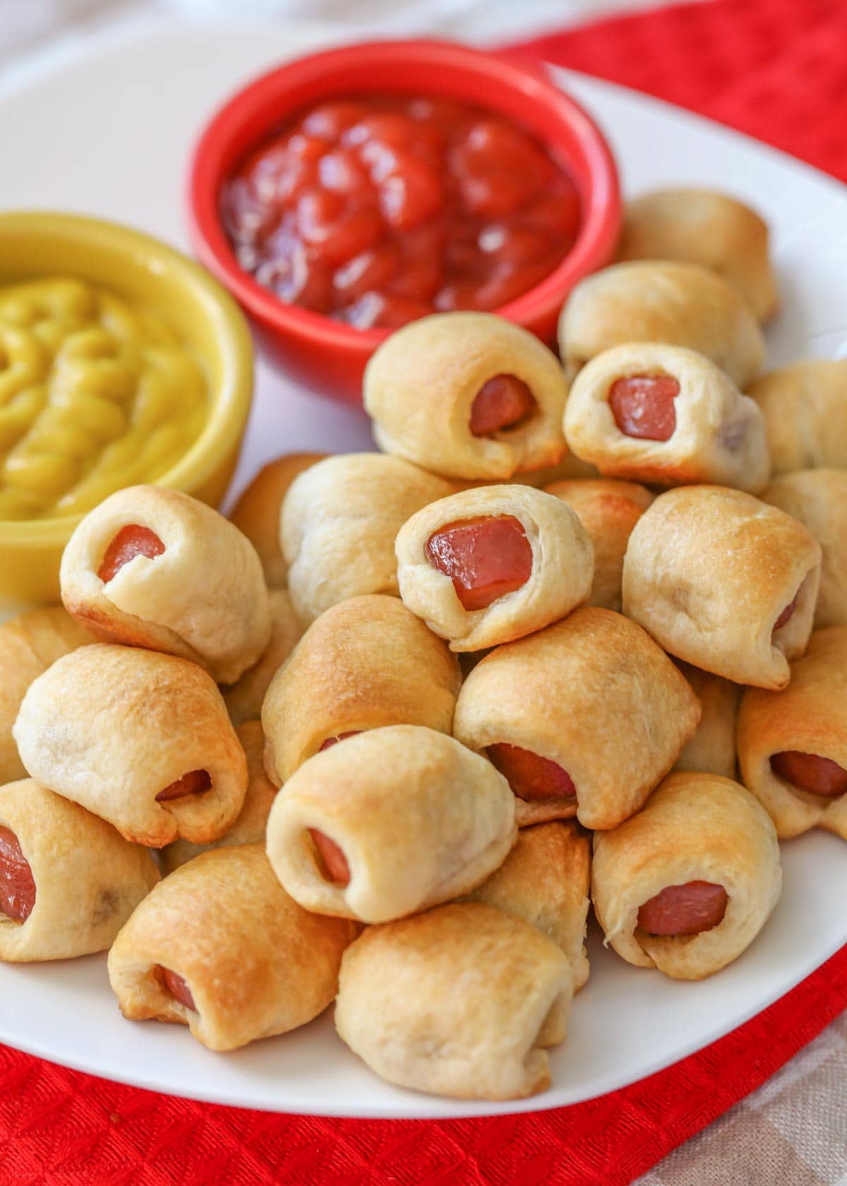 Close up of hot dog nuggets stacked on a plate with sides of ketchup and mustard